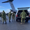 Des militaires en uniforme transportent de l'équipement depuis un camion pick-up vers des hélicoptères et un avion.