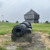 Un canon ancien est pointé vers un fort en bois construit en 1750. Le focus est sur le canon et le fort, au loin, est flou sur cette photo.