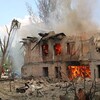 Des secouristes arrosent un bâtiment en feu, qui a été détruit en grande partie.