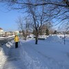 Une femme marche sur un trottoir. Elle porte une capuche, des pantalons de neige et des mitaines pour se protéger du froid.