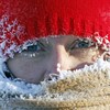 Plan rapproché de deux yeux clairs qui apparaissent entre une tuque rouge et un foulard jaune de laine couverts de neige gelée.