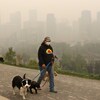 Leslie Kramer promène ses chiens non loin des immeubles du centre-ville de Calgary sous une épaisse fumée des feux de forêt.