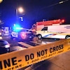 Une scène de crime, la nuit, entourée de ruban jaune de police. Plusieurs véhicules d'urgence sont sur place.