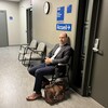 Un homme assis sur une chaise dans un corridor. 