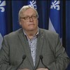 Gaétan Barrette lors d'un point de presse à l'Assemblée nationale avec des drapeaux du Québec en arrière fond