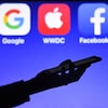 Une personne tient un téléphone devant les logos de Google, Apple, Facebook et Amazon. 