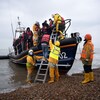 Des hommes aident des migrants à descendre d'un bateau.