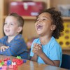 Deux enfants sont assis à une table dans une garderie, dont un qui sourit à pleines dents.