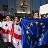 Des manifestants brandissent un drapeau de l'Union européenne et un drapeau de la Géorgie lors d'un rassemblement.