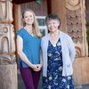 Deux femmes sourient devant un bâtiment de tradition autochtone