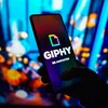 Une personne tient un téléphone intelligent montrant le logo de Giphy. 