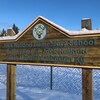 Panneau de bois en trois langues annonçant l'École primaire Jack-Hulland, à Whitehorse, à l'hiver 2022.