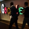 Deux personnes marchent devant le logo de Google.