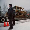 Des policiers laissent passer de la machinerie sur une route de terre. 