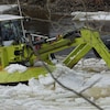 Une pelle mécanique flottante verte brise la glace dans la rivière.