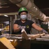 Une femme d'origine philippine manipule des pièces de bois sur une machine dans l'usine.