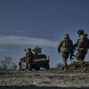 Trois soldats dans un champ austère de dos se dirigent vers leur véhicule armée d'une tourelle. 