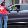 Une dame dans une voiture fait un don à une bénévole de la guignolée.