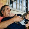 Un homme d'un certain âge est assis sur la véranda en tenant sa guitare et regarde dans le néant d'un air vitreux.