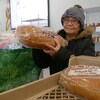 Erlinda De Guzman tientu pain dans ses mains, à côté de son sac rempli de denrées. Elle est dans le local de Harvest Manitoba et on peut voir autour d'elle des tablettes remplis de produits. 