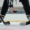 Un arbitre dépose une rondelle sur la glace devant deux joueurs de hockey.