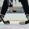 Un arbitre lance une rondelle sur la glace devant deux joueurs de hockey. 