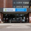 Une personne assise sur un banc devant l'Hôpital de Moncton.