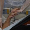 Plan rapproché du bras d'un patient couché dans un lit d'hôpital. Une infirmière lui tient la main.