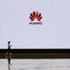 Une femme marche devant un écran blanc sur lequel est projeté le logo de la compagnie Huawei.