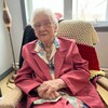 Une personne âgée assise sur un divan, souriant à la caméra.