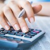 Une personne tenant un stylo dans sa main semble taper des numéros sur une calculatrice. 