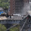 Deux grandes échelles de pompier dirigées vers une section du bâtiment d'où émerge une colonne de fumée.