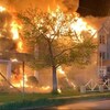 D'importantes flammes couvrent des logements, et on voit l'avant d'un camion de pompiers.