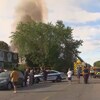 Des résidents du quartier observent la scène alors qu'une épaisse colonne de fumée s'élève au-dessus d'une maison.