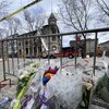Des fleurs déposées près d'une barrière en métal devant un édifice incendié.