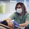 Une infirmière qui porte le masque sanitaire ajuste le masque d’un respirateur artificiel sur le visage d’une patiente couchée dans un lit d’hôpital. 