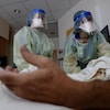 Deux infirmières penchées au-dessus d'un homme dont on ne voit que le bras gauche, couché sur un lit d'hôpital.