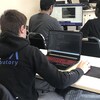 Un étudiant travaille sur un logiciel de programmation. Il est assis dans une salle de classe.