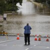 Un homme se tient devant une rue fermée et complètement inondée. 
