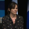 Une femme au micro avec des drapeaux du Québec derrière elle.