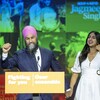 Jagmeet Singh lève le poing en souriant. Il tient la main de son épouse devant un podium où est écrit le slogan « Fighting for you; Oser ensemble ».