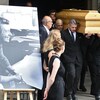 Des porteurs de cercueil sortent d'une église, devant laquelle est installée une photographie en noir et blanc de Jean-Jacques Sempé.