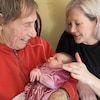 Un homme tient un bébé dans ses bras, alors qu'une femme touche au visage du bébé.