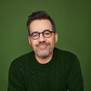 Portrait de l'animateur et humoriste souriant, sur un fond vert.