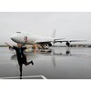 Jeannie Boisvert lève les bras sur le tarmac d'un aéroport devant un avion gros porteur.