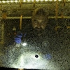 Un homme examine une vitre fracassée d'un autobus.