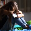 Une jeune fille se tient la tête dans les genoux avec son téléphone intelligent à la main.