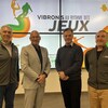 Quatre hommes posent pour la caméra en souriant devant l'affiche montrant le slogan Vibrons au rythme des Jeux.