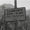 Enseigne avec l'inscription : Chamonix Mont-Blanc ville olympique. On voit des montagnes enneigées en arrière-plan.