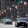 Des voitures de police dans une rue du centre-ville d'Ottawa où l'on voit des drapeaux canadiens et américains suspendus aux lampadaires.